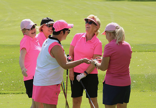 Group of women in on golf course, wearing pink golf attire.