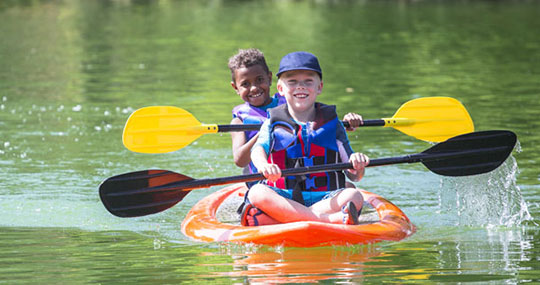 Two young boys smile while paddling a paddleboard together. 