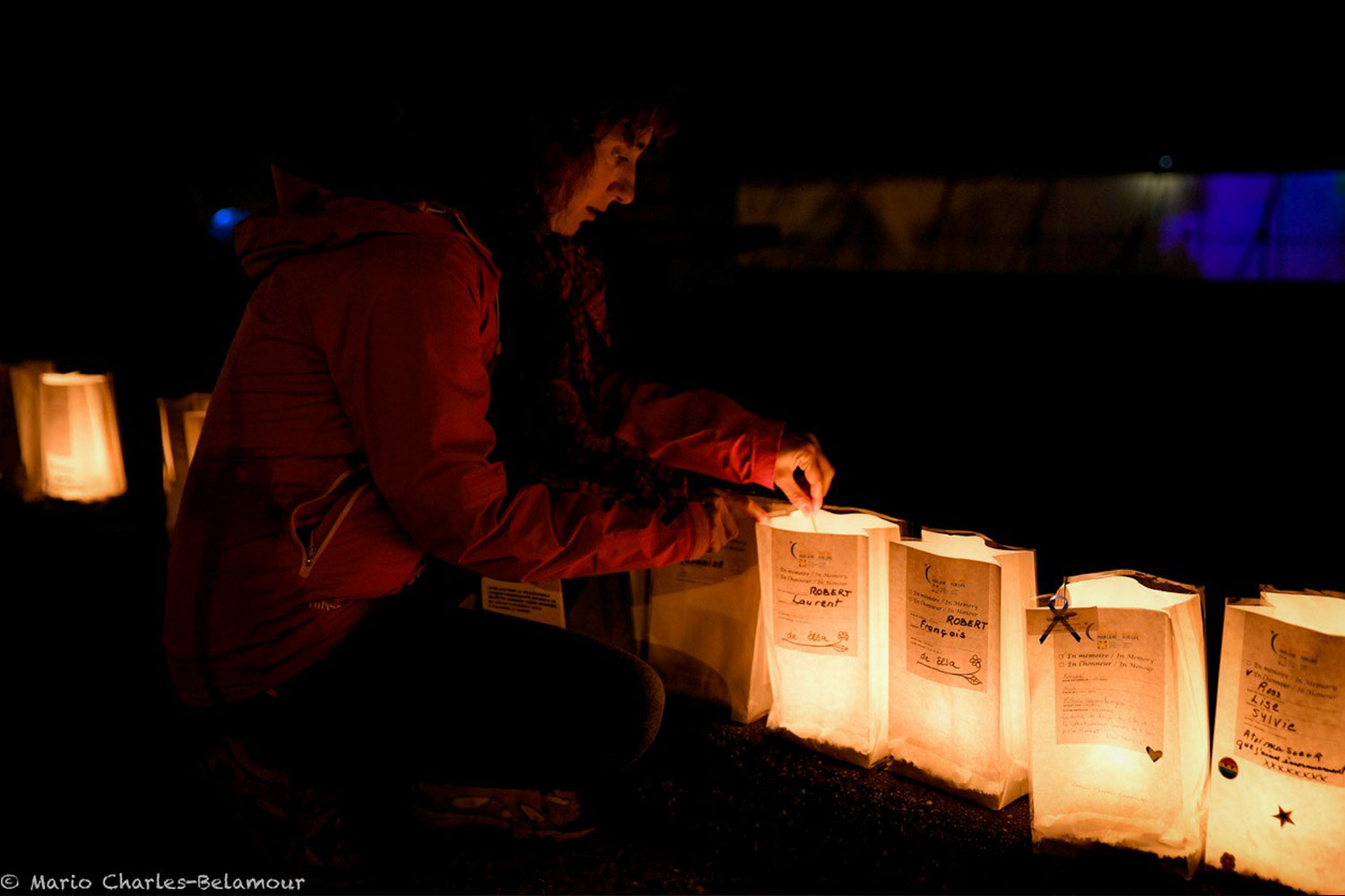 A woman sitting on the ground, lighting a luminary. 