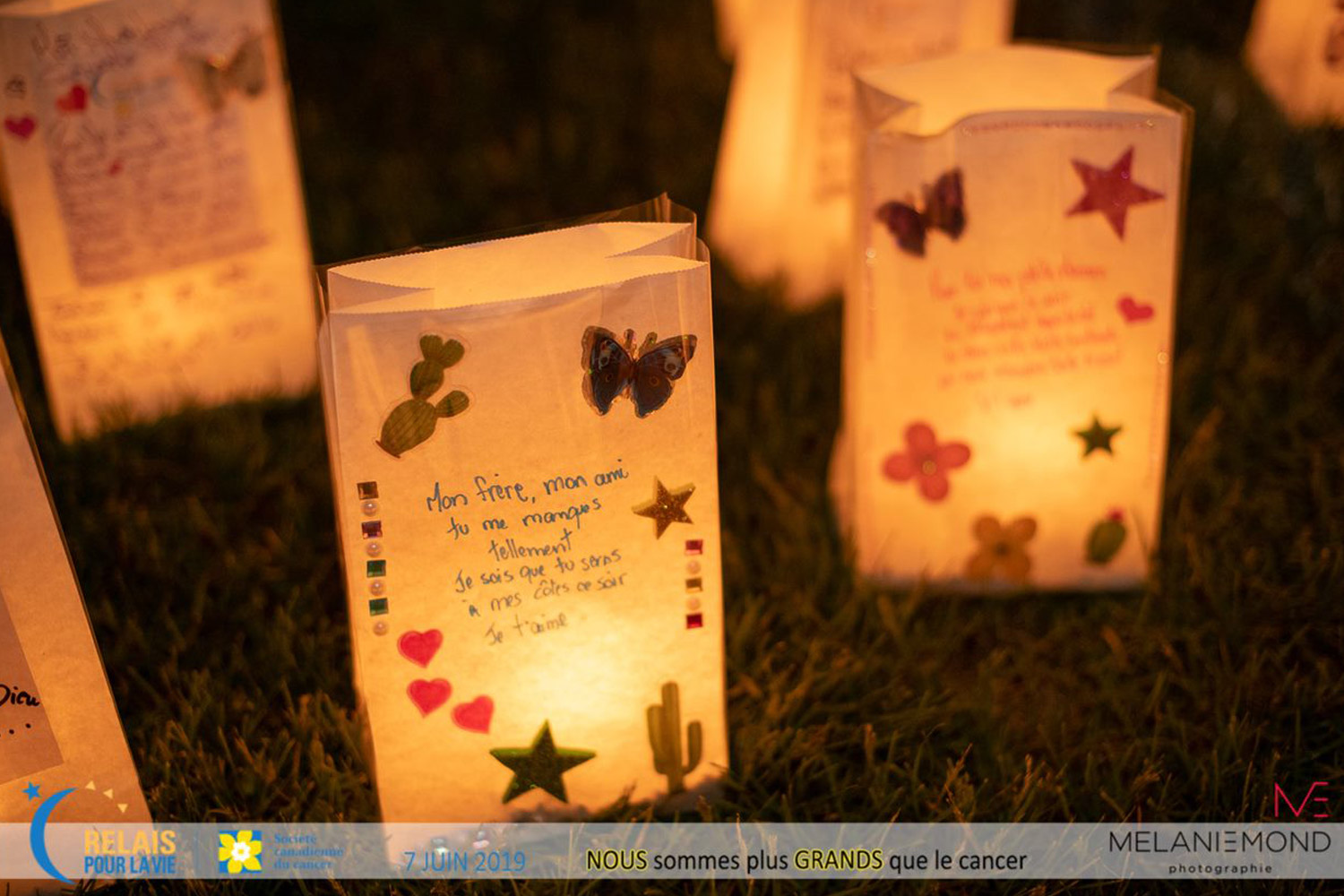 Glowing luminaries sit on the ground with written messages on them.