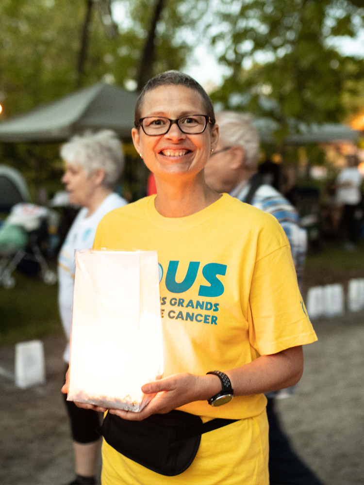  A woman wearing a Relay shirt, smiling, and holding a luminary.