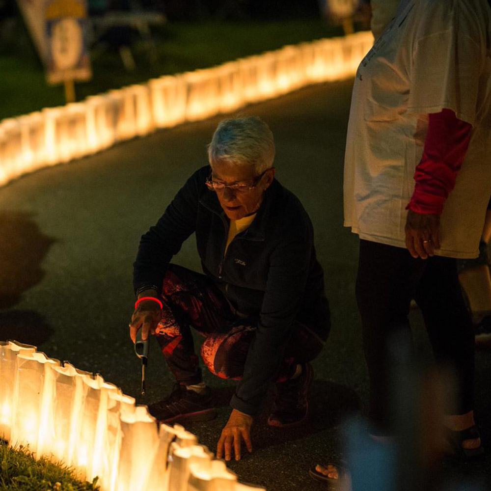 An older adult crouching and lighting a luminary.